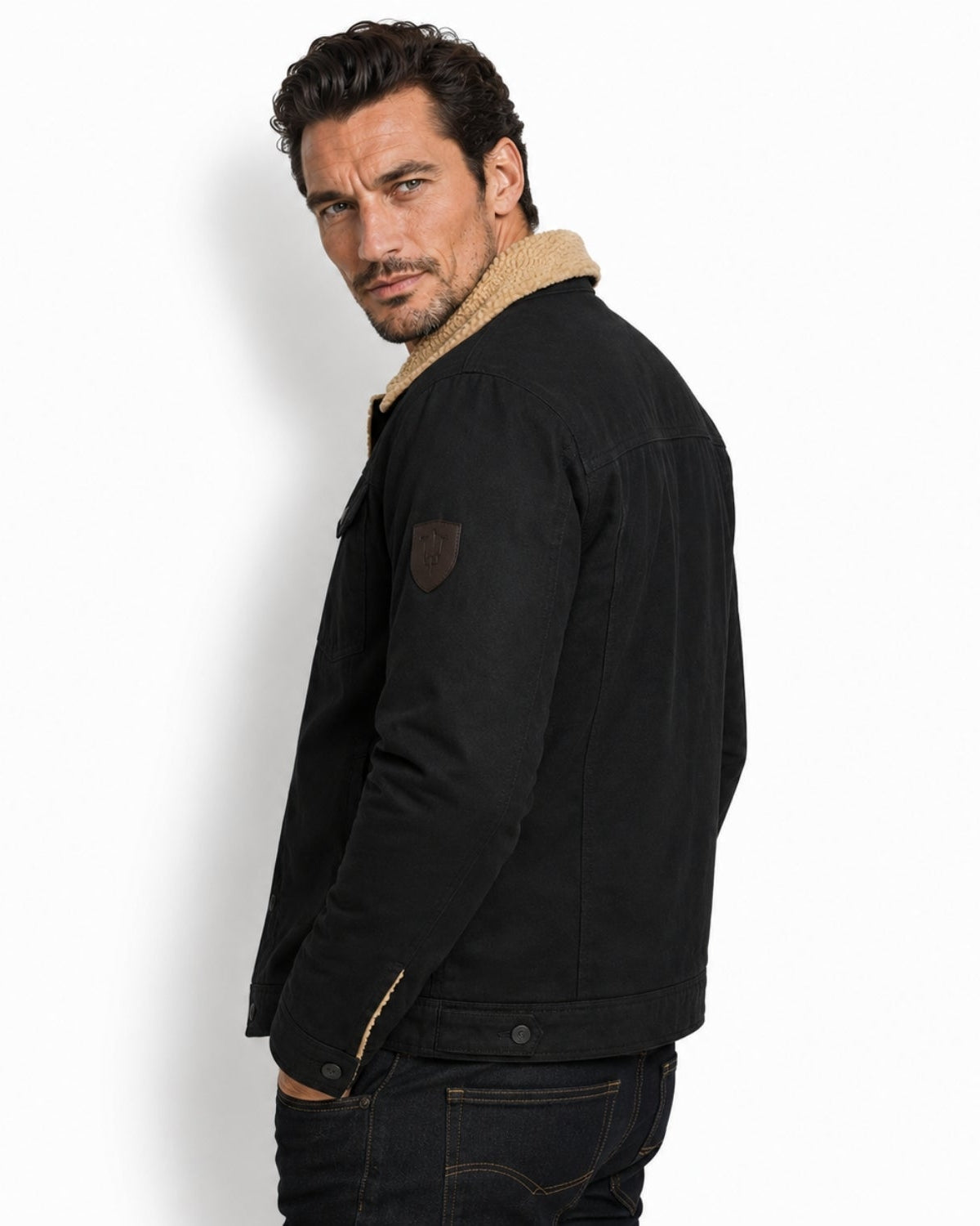 Side profile of men's luxury black trucker jacket showcasing reinforced stitching, dark metal hardware, and sleeve patch detail.