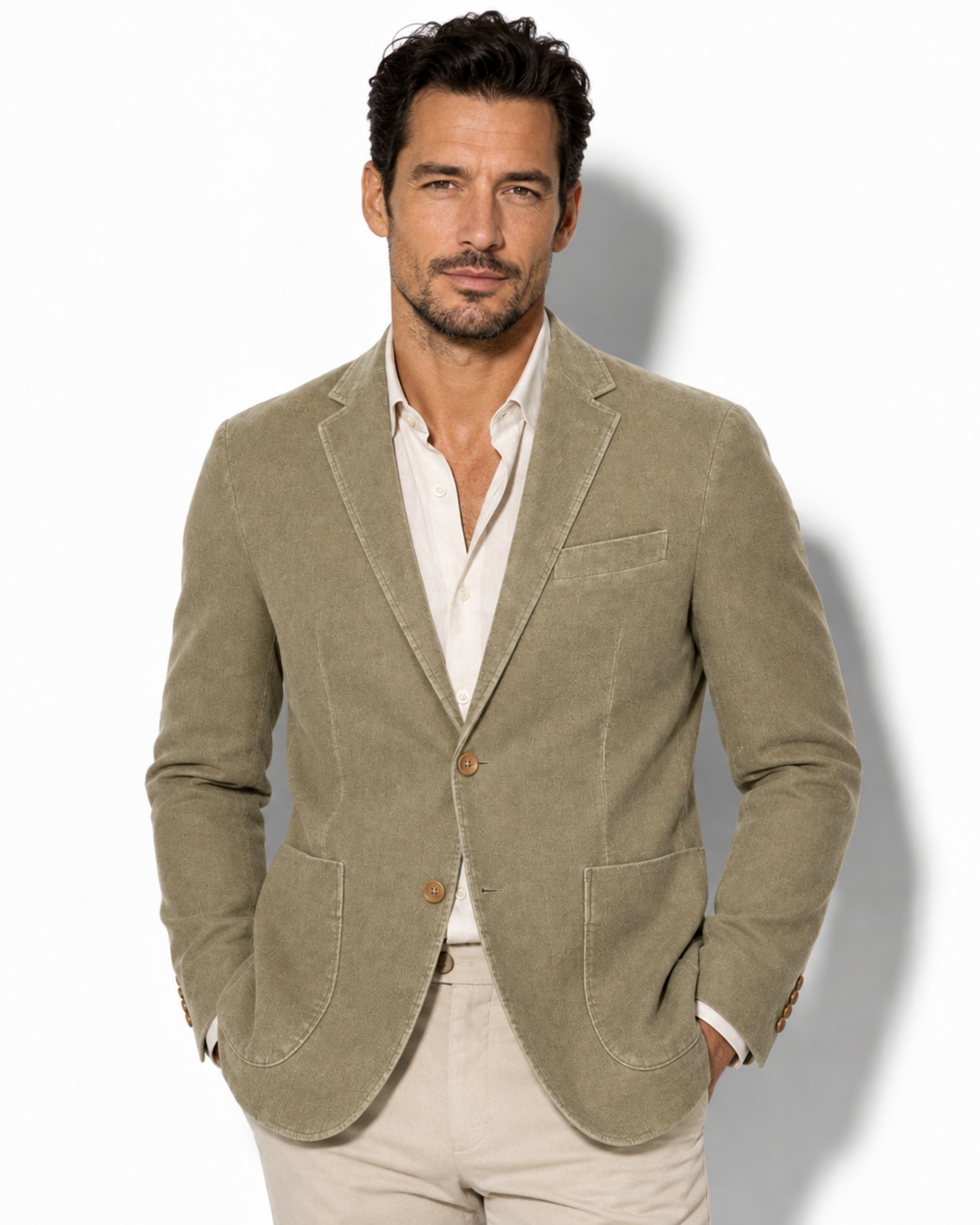 A handsome man wearing a tailored men's green corduroy blazer, featuring an unstructured fit and patch pockets, over a white linen shirt.